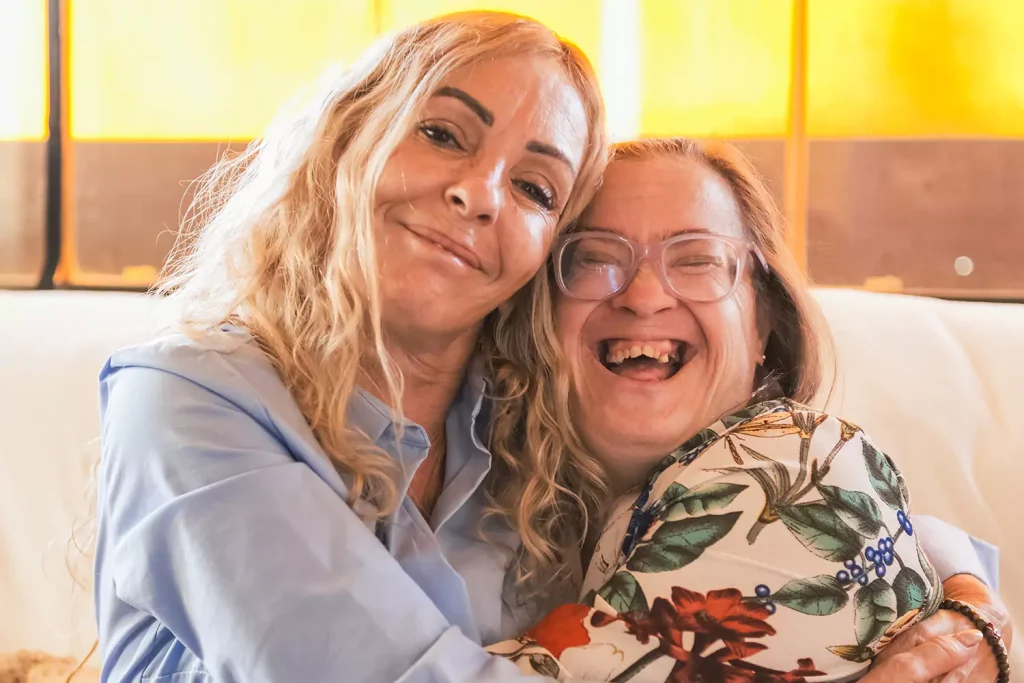 A woman with down syndrome is smiling while hugging her care provider