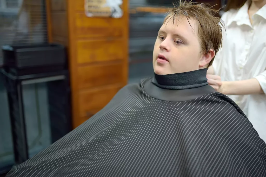 A young man with down syndrome is receiving a haircut from the barbershop