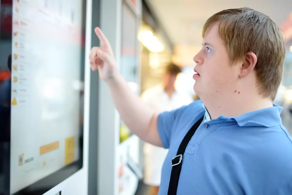 A young man with down syndrome is selecting a meal via a touch screen at a takeaway shop