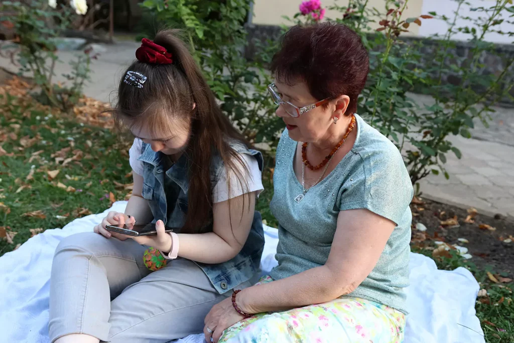 A young woman with a disability is using her phone while sitting with her care provider