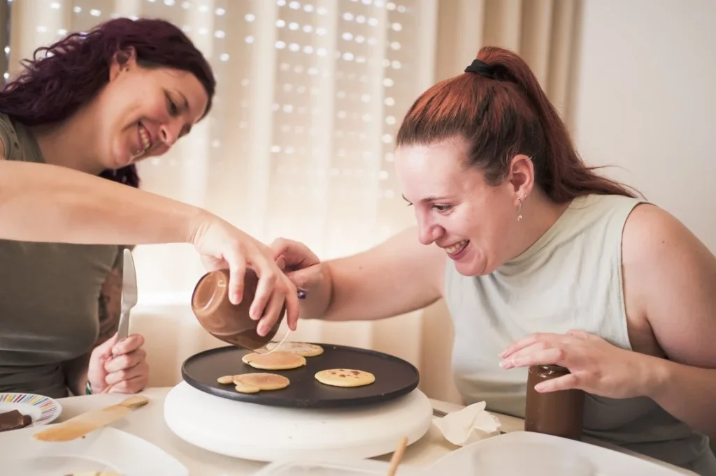 Two women are smiling while making pancakes together