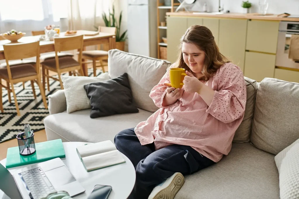 A young woman with down syndrome is enjoying a cup of coffee of the couch