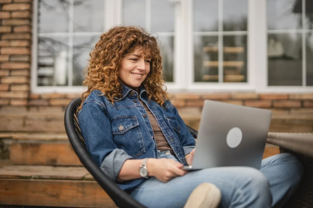 A woman is smiling while using her laptop to make NDIS referrals