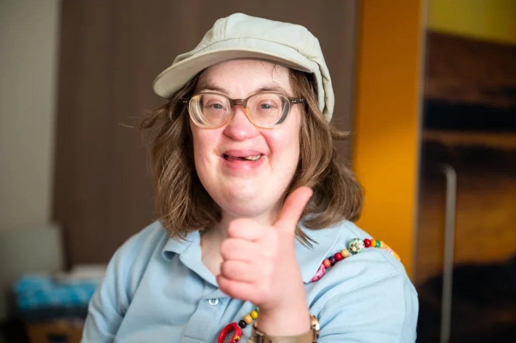 A woman with down syndrome is smiling while giving thumbs up